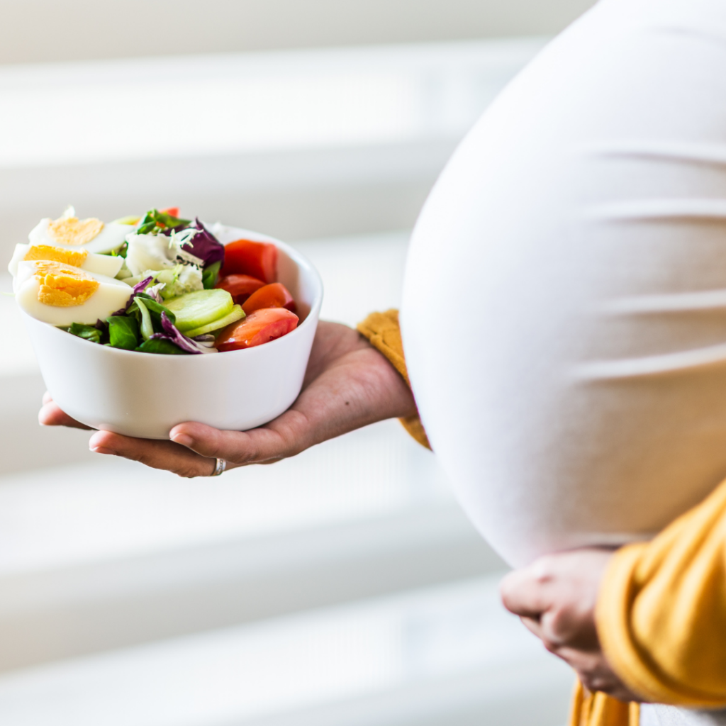 A pregnant woman with her baby bump holding a bowl of nutritious salad, proof that this is one of the more common menopause myths - you can get pregnant in perimenopause!