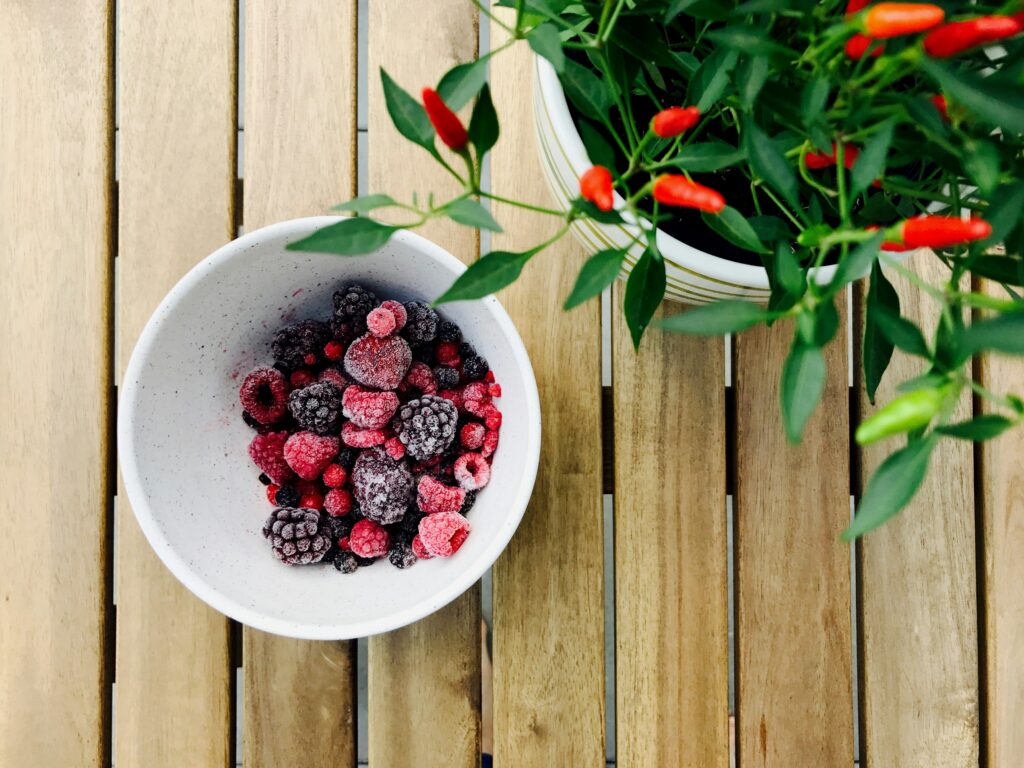 A bowl of blackberries and raspberries as berries are foods to stop sugar cravings. Next to the bowl is a chilli plant.