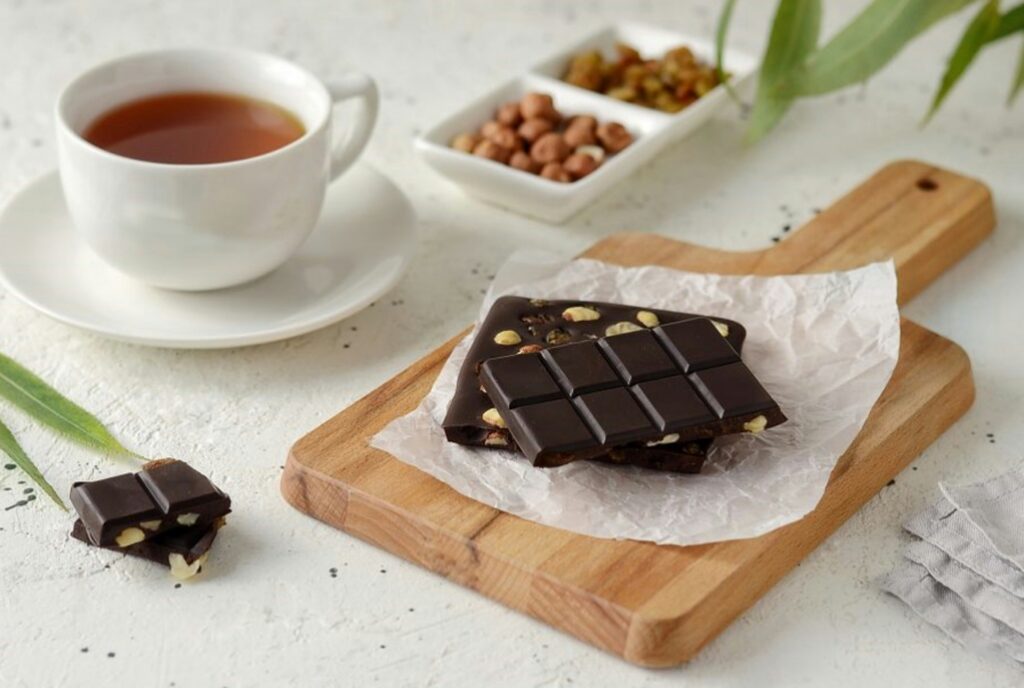 One of the foods to stop sugar cravings - dark chocolate with nuts on a chopping board next to a cup of tea and more nuts.
