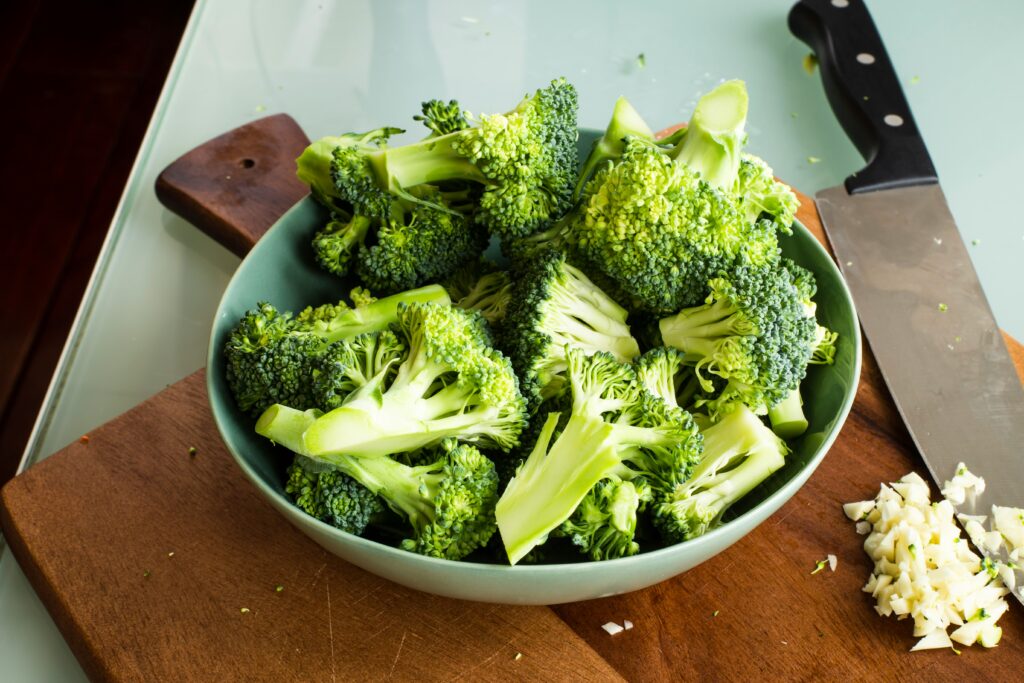 A knife, chopping board and a bowl full of one of the best foods for skin - broccoli florets.