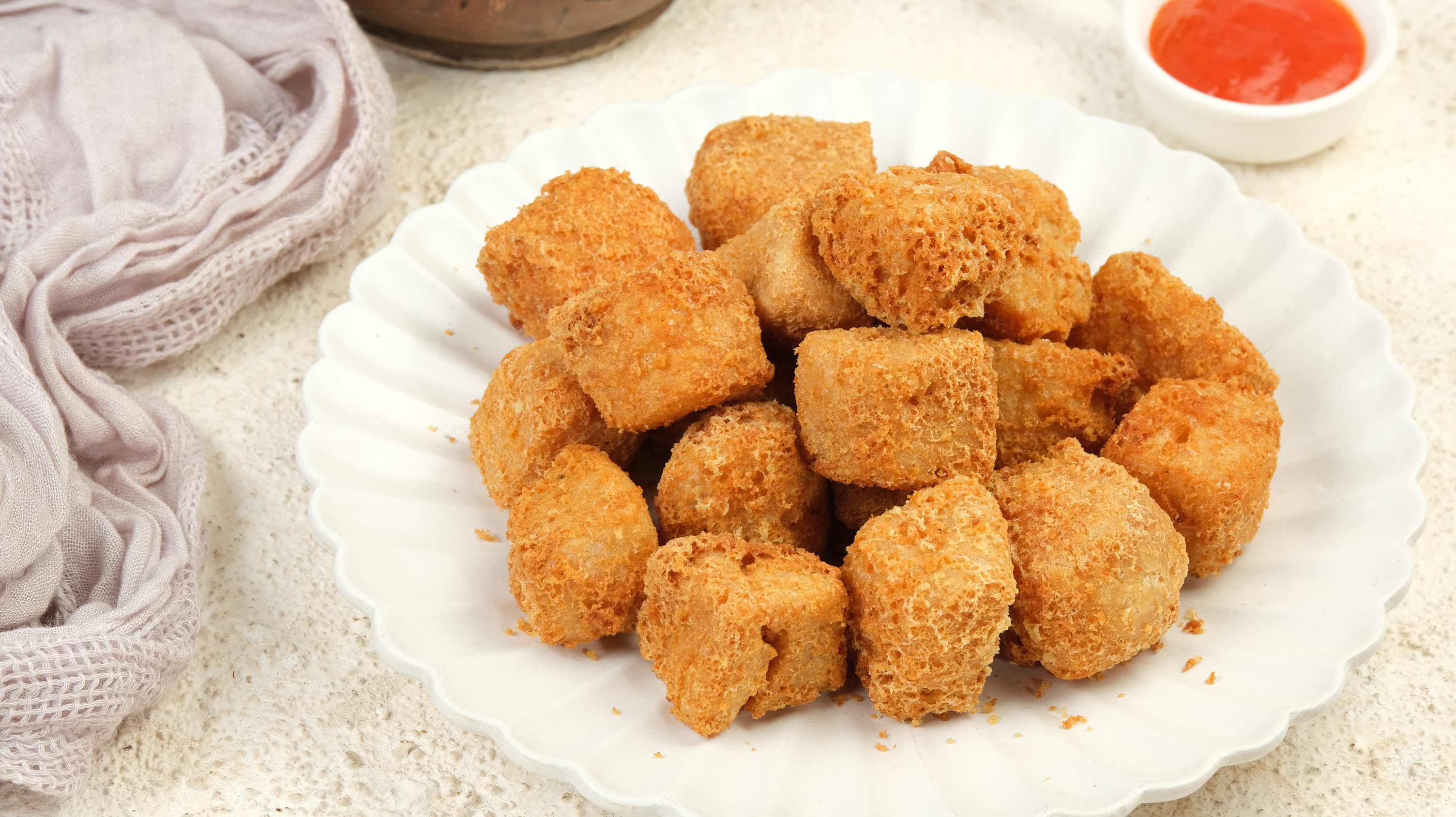 A plate of air fryer tofu - popcorn/nugget style. A little pot of ketchup is in the background for dipping.
