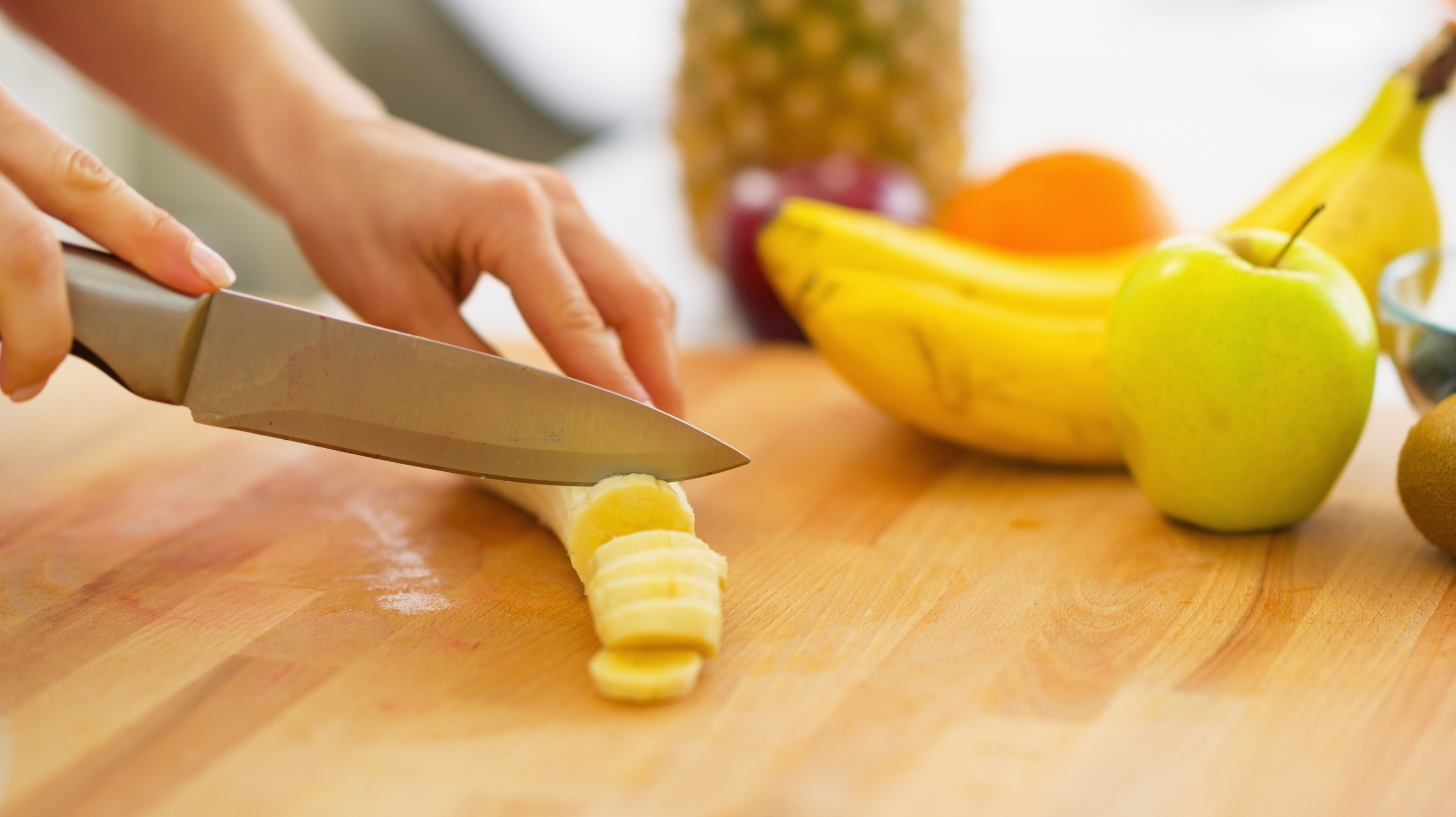 Someone cutting a banana on a chopping board with a kitchen knife. An apple is in front of the banana. Chopping the best foods for perimenopause.