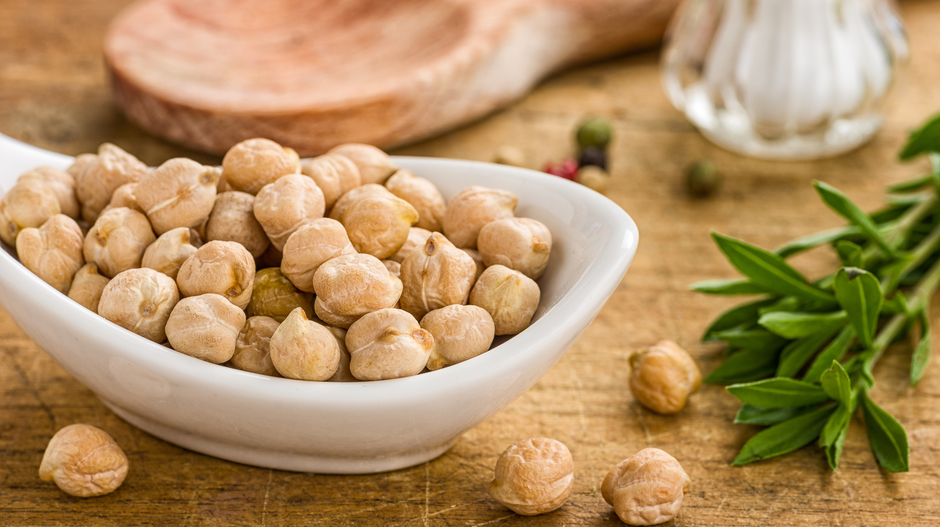 A bowl of chickpeas that are full of fibre as one of the better foods for perimenopause. Next to the bowl of chickpeas is a sprig of herbs with a wooden spoon and some garlic in the background.