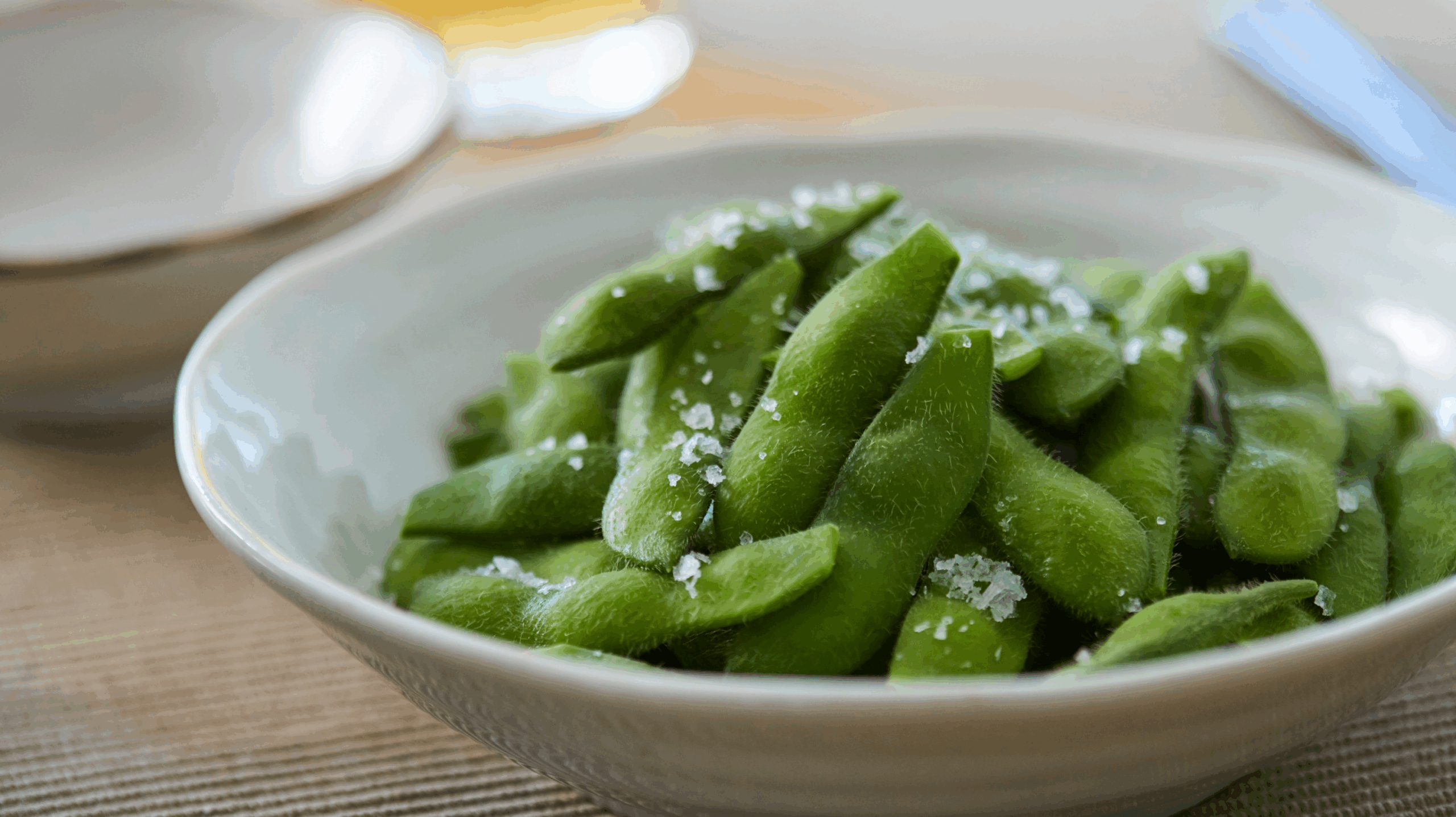 A bowl full of edamame beans on a lined place mat, sprinkled with salt. One of the better snacks and foods for perimenopause
