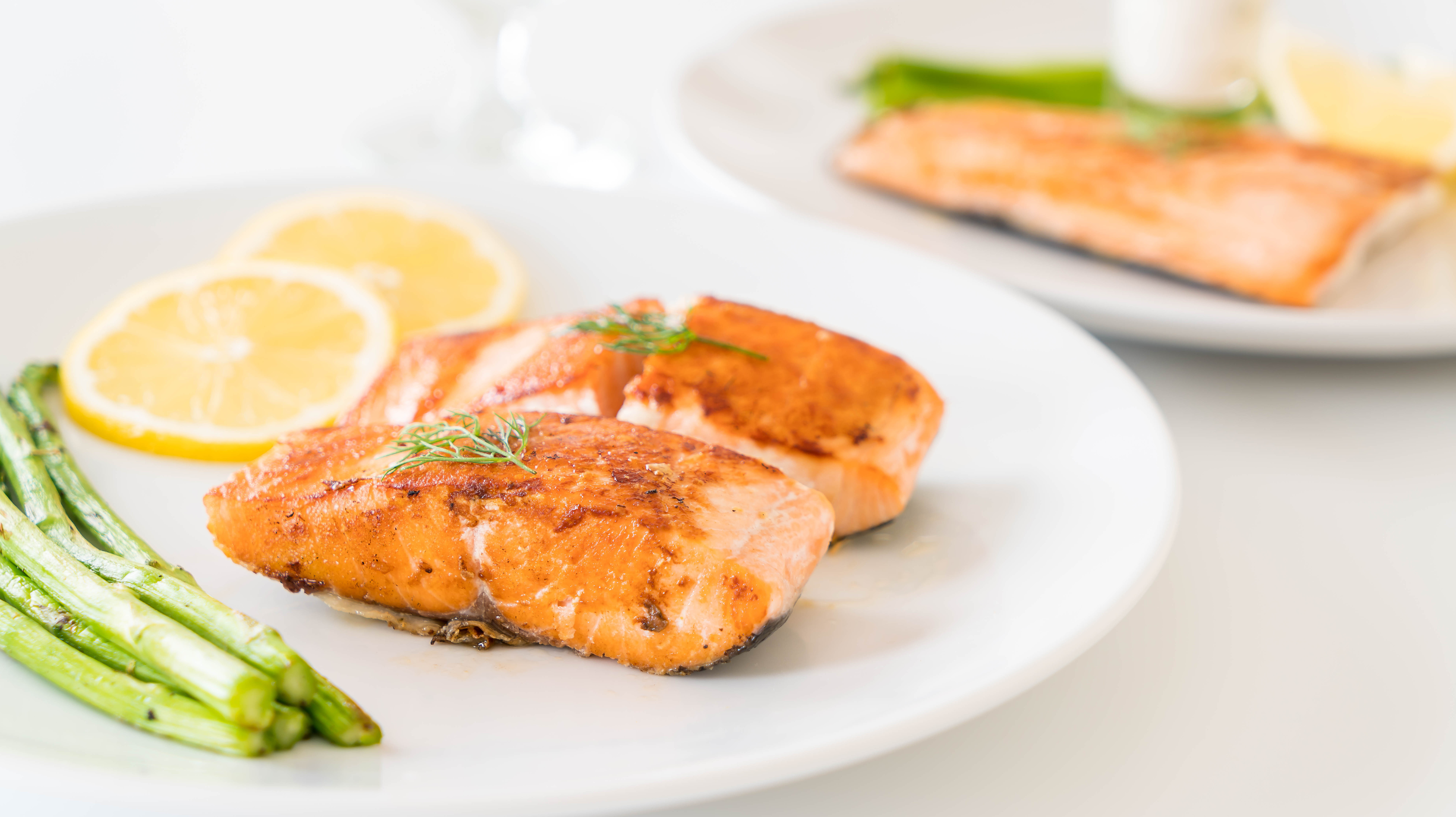 A dish of cooked salmon topped with dill, two slices of lemon and a side of asparagus. Salmon is a healthy source of protein, making it a great choice for foods for perimenopause