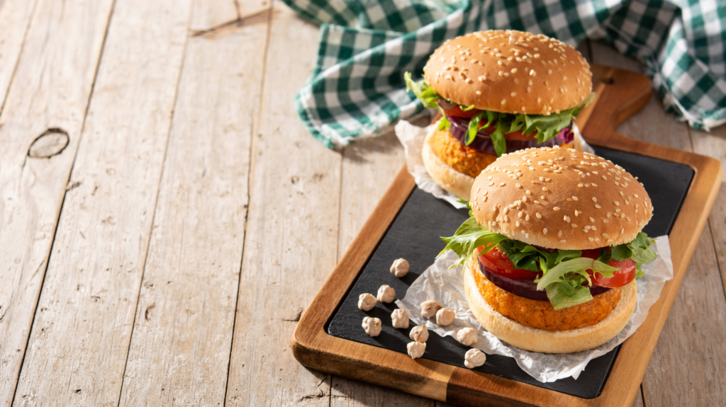 A firm favourite of our chickpea recipes - a chickpea burger on a board with red onion, lettuce and tomatoes.