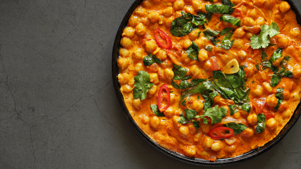 A bowl of one of the most delicious chickpea recipes ever - a chickpea and spinach curry in a black bowl on top of a marbled grey worktop. 