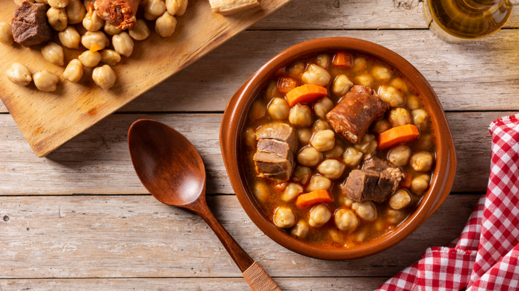 Chickpea recipes in all their glory with this bowl of Spanish chorizo and chickpea stew. A wooden spoon sits next to the bowl on a wooden table.