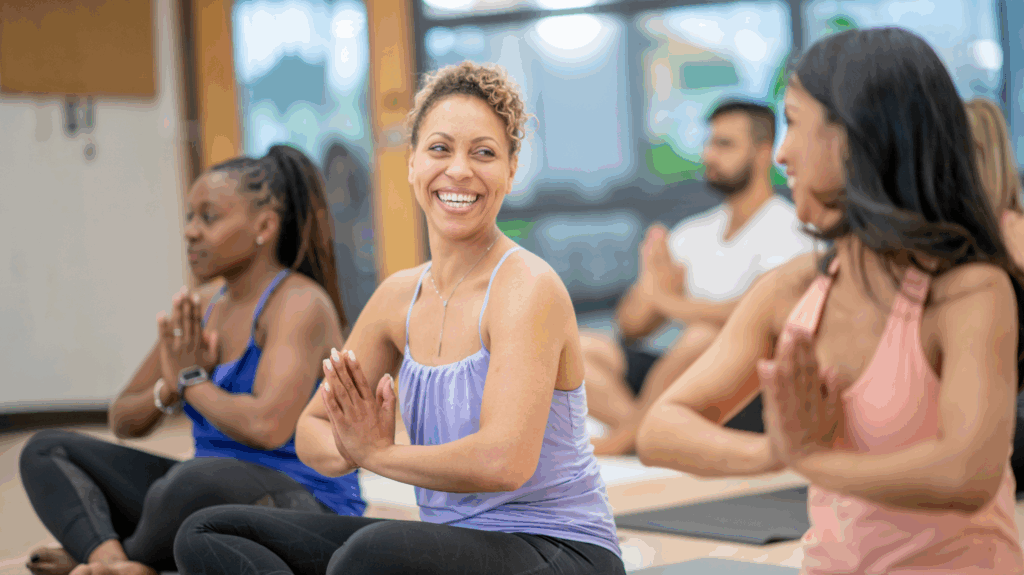 Three women and a man in a yoga class, smiling at each other. Women are there for overall symptoms but particularly menopause bloating