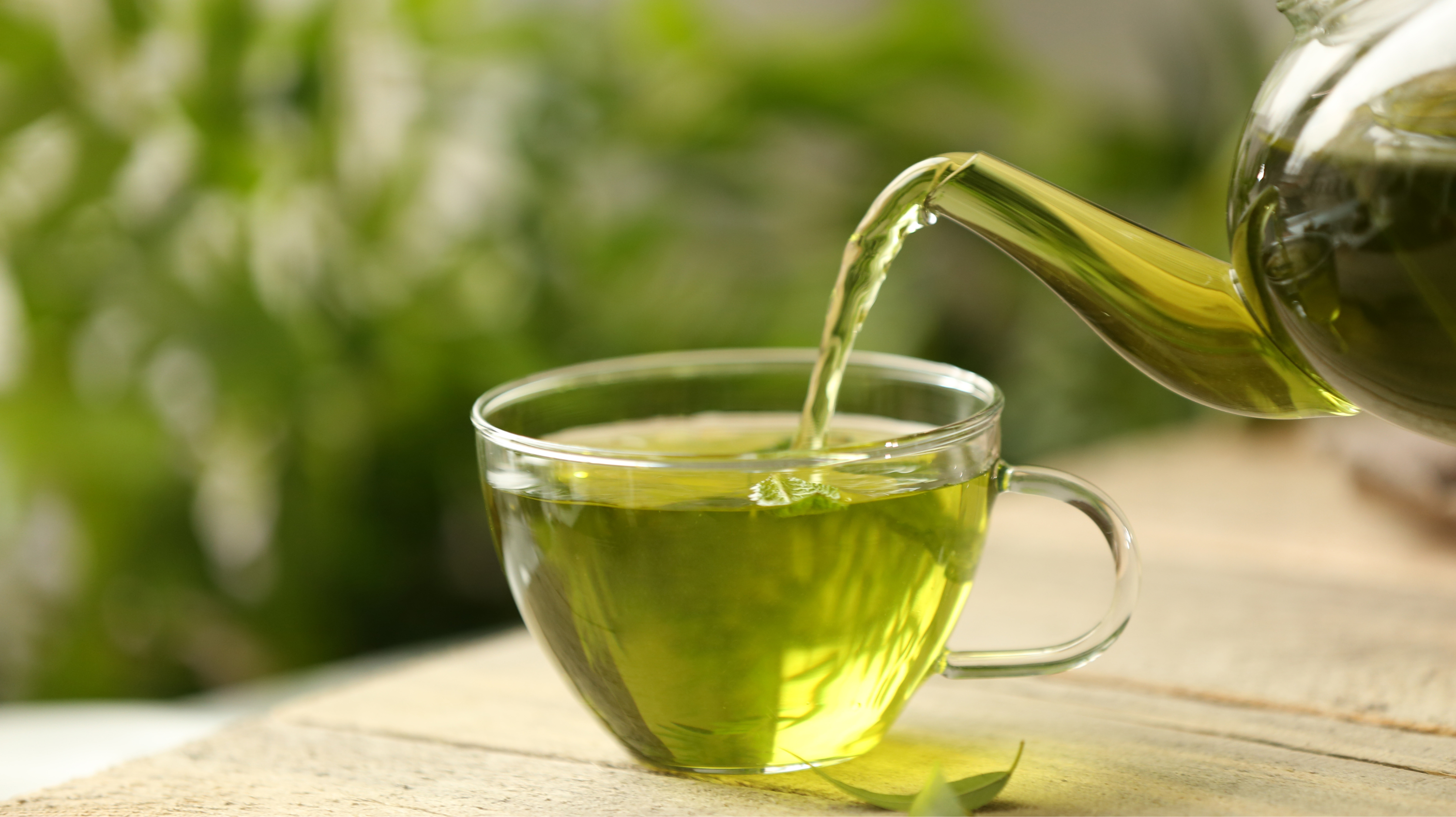 A clear mug with a clear teapot pouring green tea into the mug on a table. This green tea will help with breast tenderness in menopause.