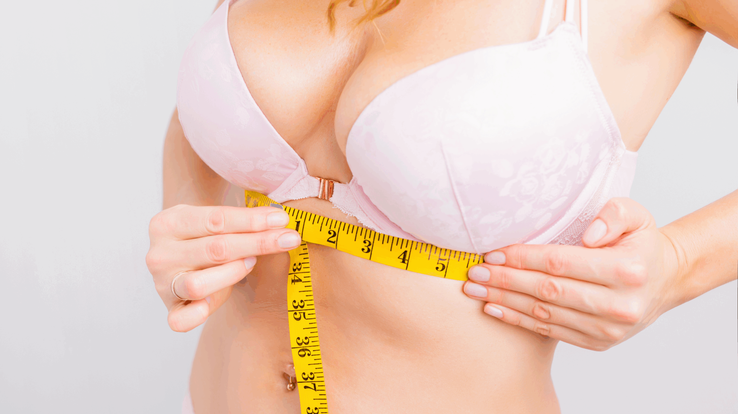 A woman in a pink bra with a measuring tape, measuring for a better bra size to tackle breast tenderness in menopause