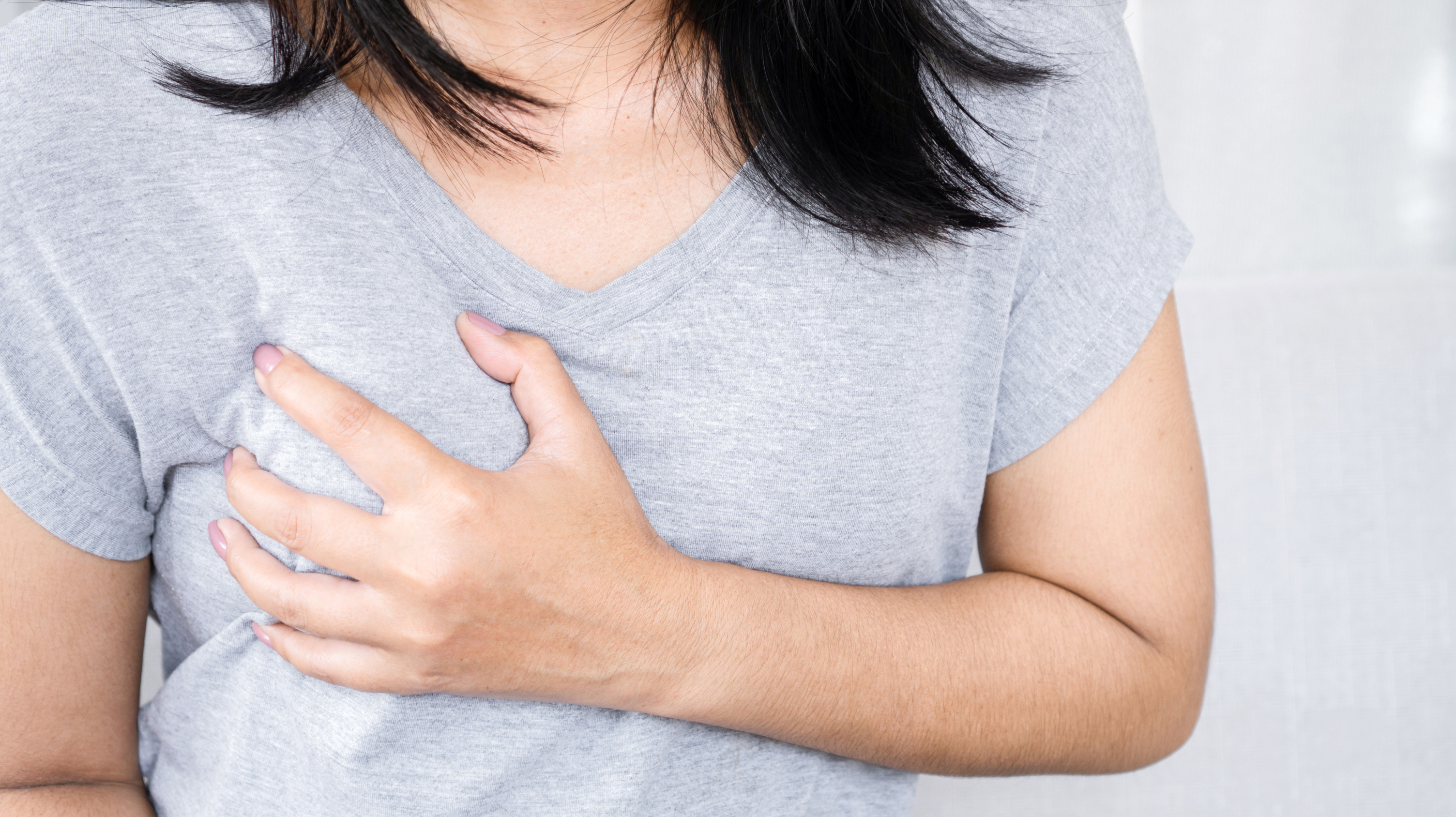 Woman with shoulder-length black hair, wearing a grey top clutching her breast due to suffering from breast tenderness in menopause