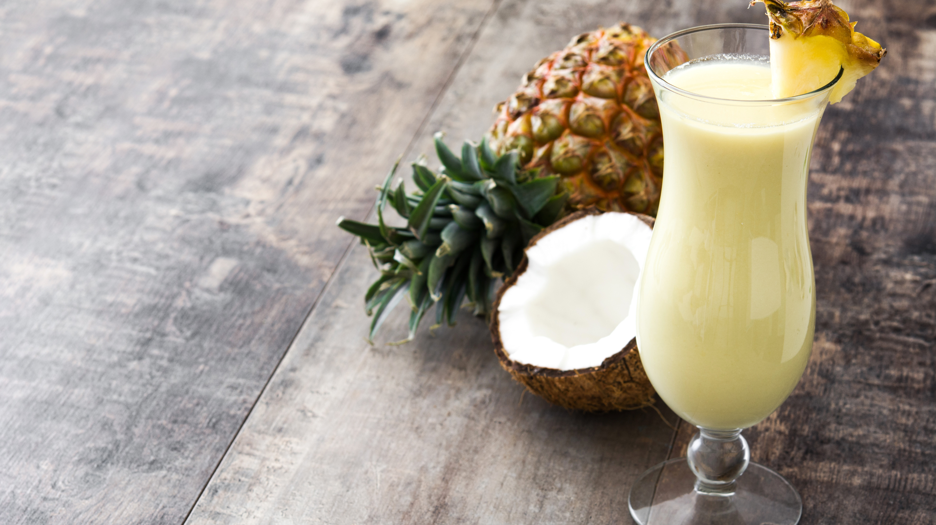 A glass of one of everyone’s favourite mocktail drinks - a virgin pina colada - with a coconut and pineapple in the background