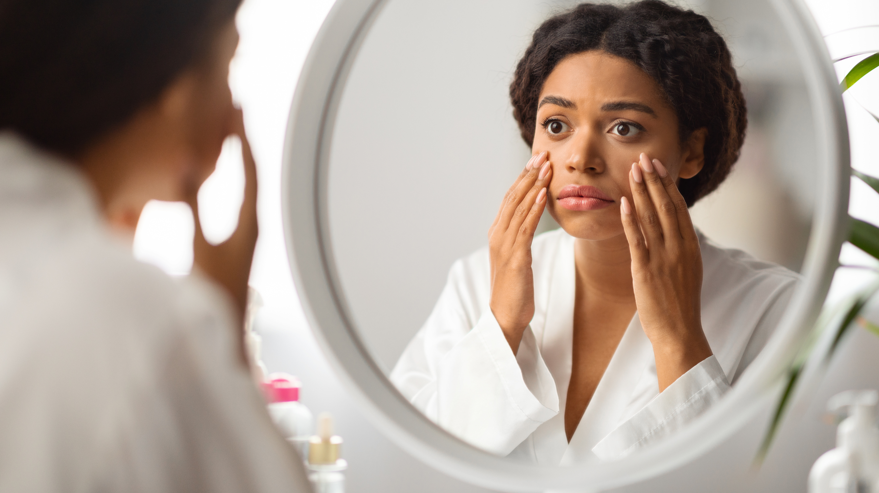 Woman in a dressing gown looking in the mirror at her perimenopause skin problems - dull complexion during perimenopause.
