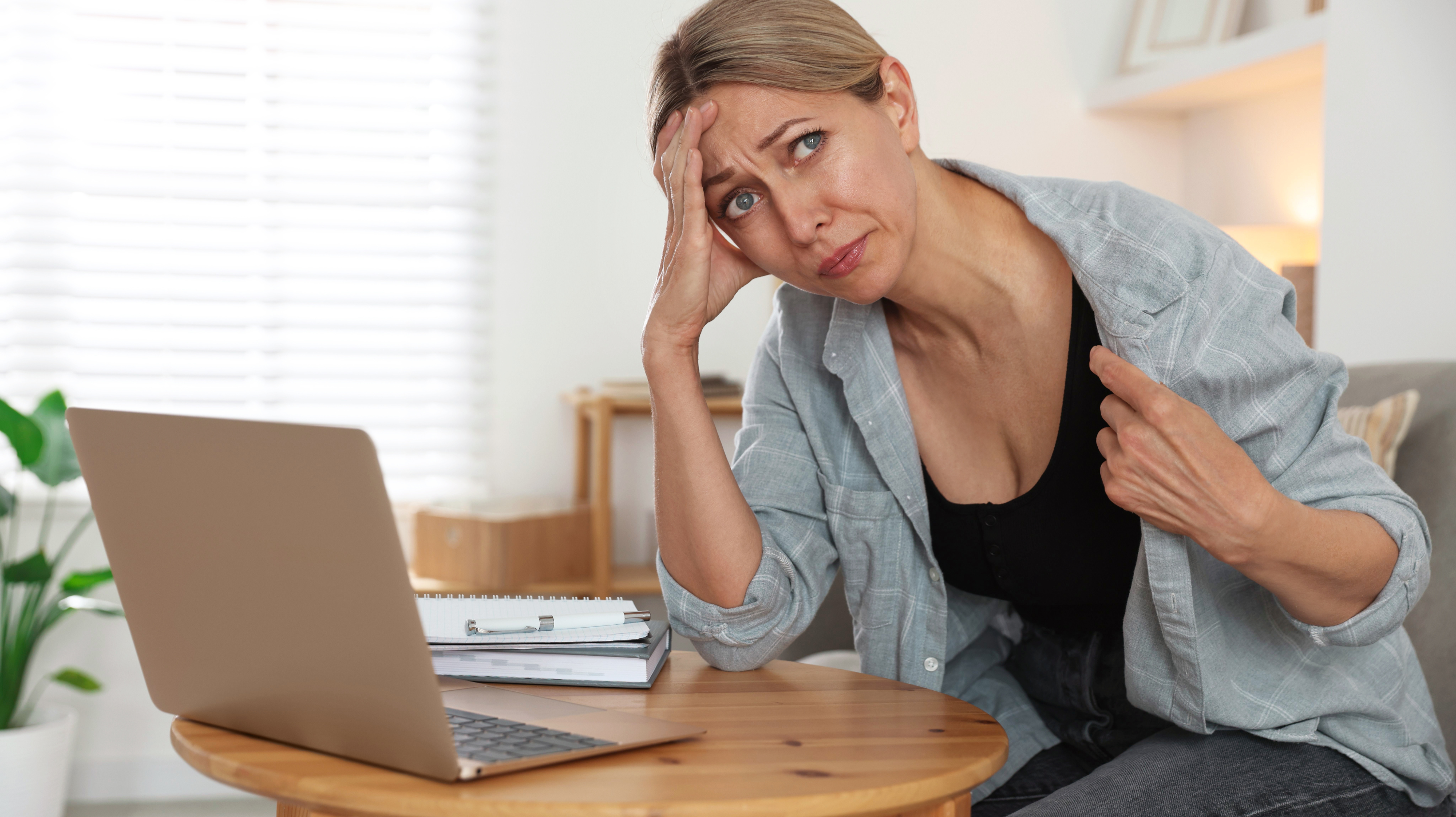 Woman trying to work in her living room but having a hot flash in perimenopause, changes to hot flashes and night sweats are signs perimenopause is ending