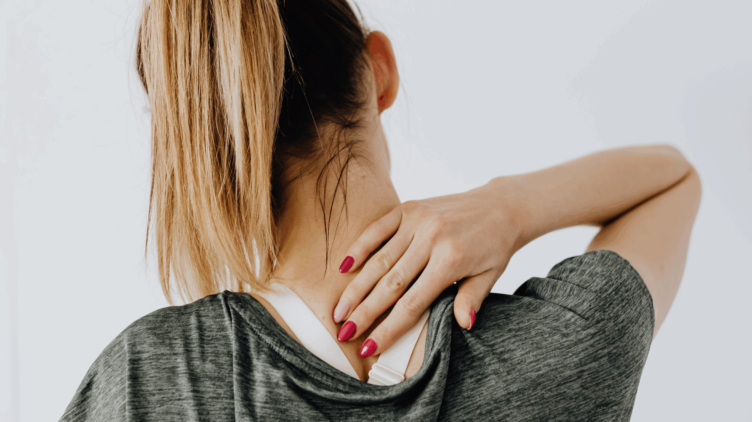 Woman with her hair in a ponytail rubbing the back of her neck due to pain, in need of supplements for joint pain.
