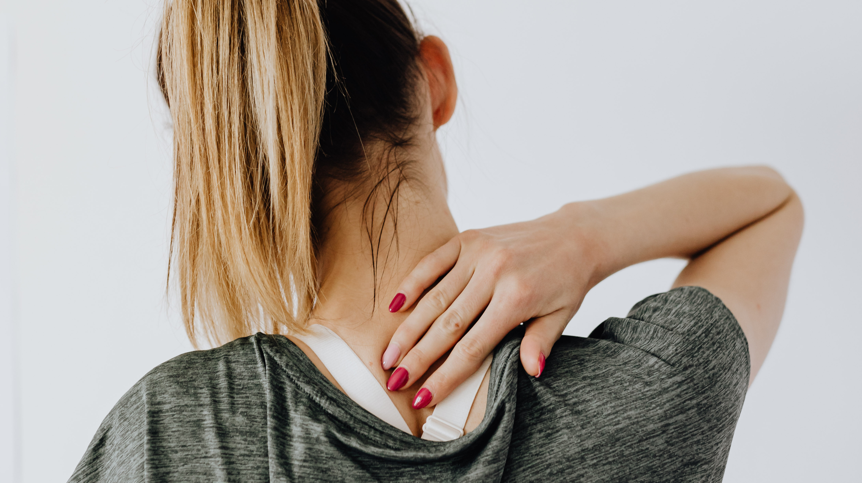 Woman with her hair in a ponytail rubbing the back of her neck due to pain, in need of supplements for joint pain.
