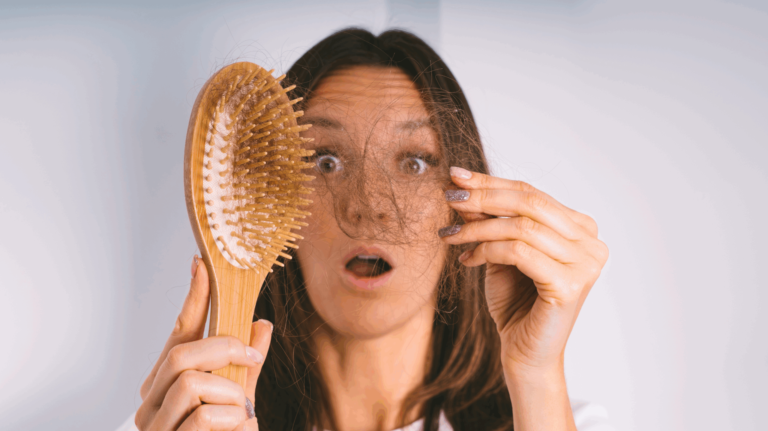 A woman experiencing perimenopause and hair loss. She’s looking at her hair brush to see how many strands of hair she has lost.