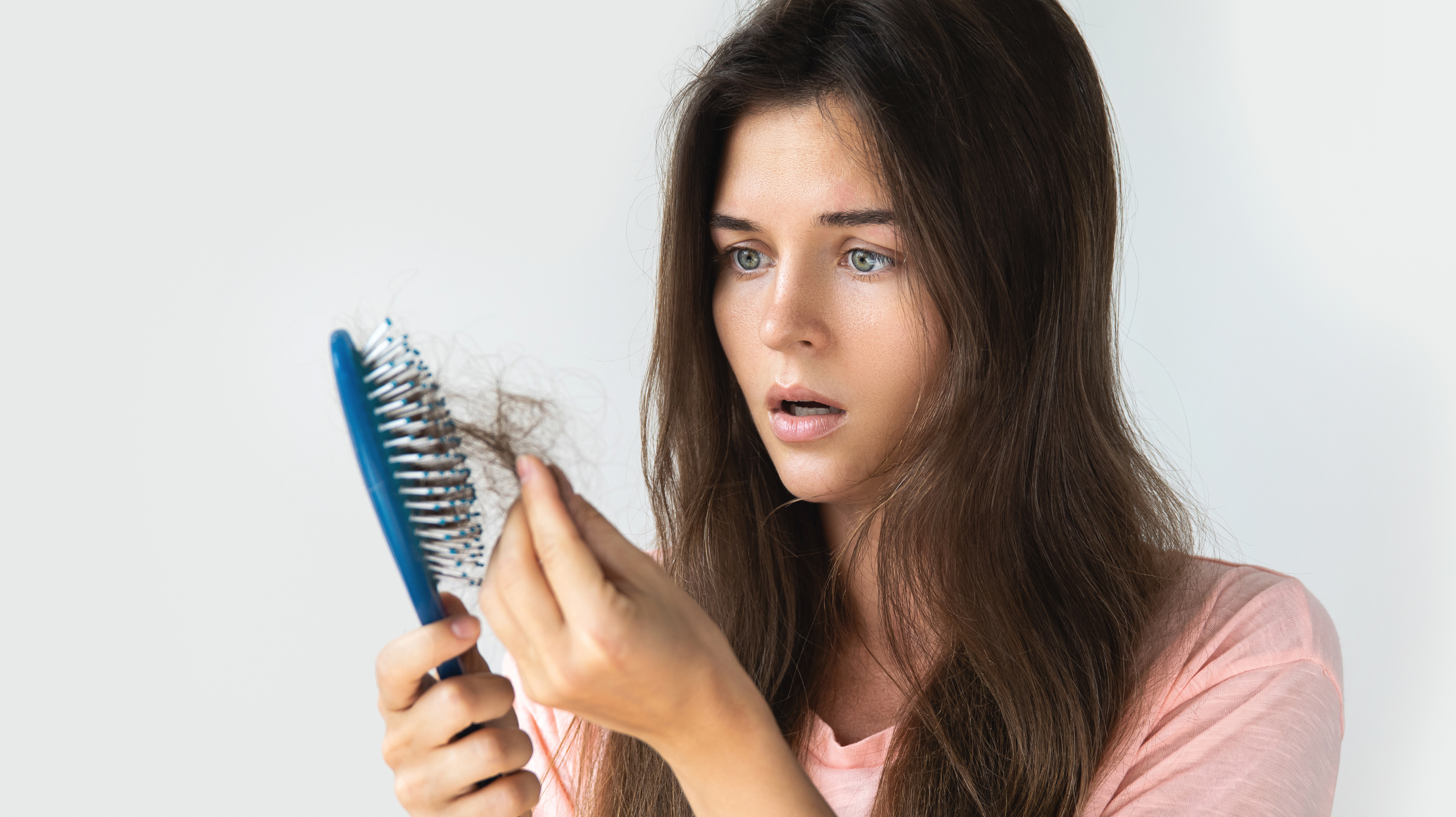 Woman with brown hair and blue eyes holding a hair brush which contains clumps of her hair due to hair loss in premature menopause