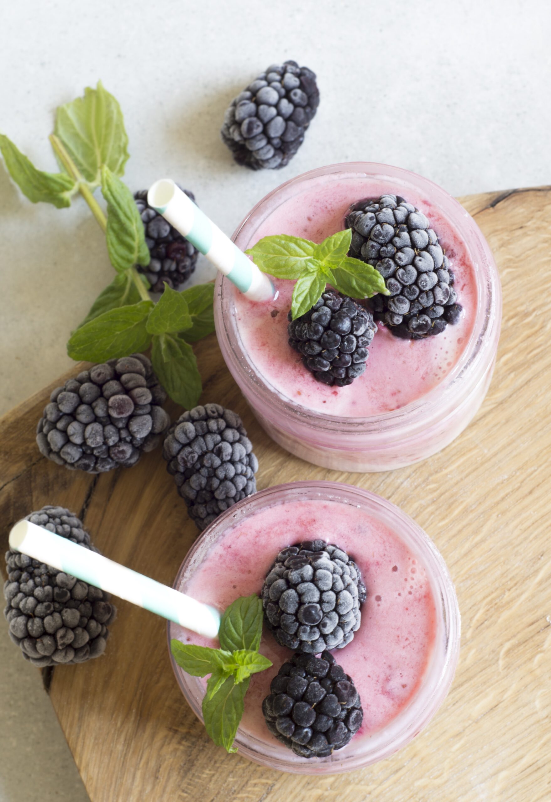 Two berry smoothies shown from a birds eye view with frozen black berries